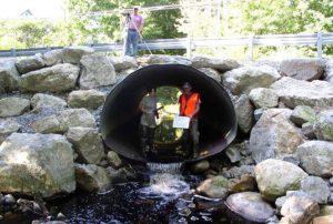 Three surveyors stand at the outlet of a stream crossing looking at the connection between outlet perch and outlet pool.