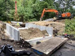 Photo of construction site of a new box culvert installation. The photos shows a large excavator moving soil to install the culvert. 